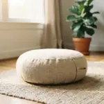 Round linen floor cushion resting on a textured rug in a room with a plant and bookshelf